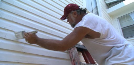 Painter painting siding with brush.