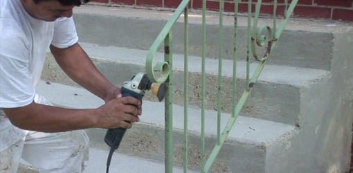 Using grinder with wire brush to remove rust from metal handrails.