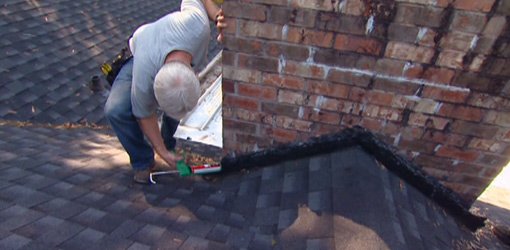 Applying roofing cement to flashing around chimney.