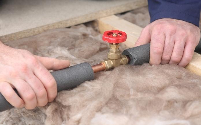 Hands holding foam insulation on a water pipe