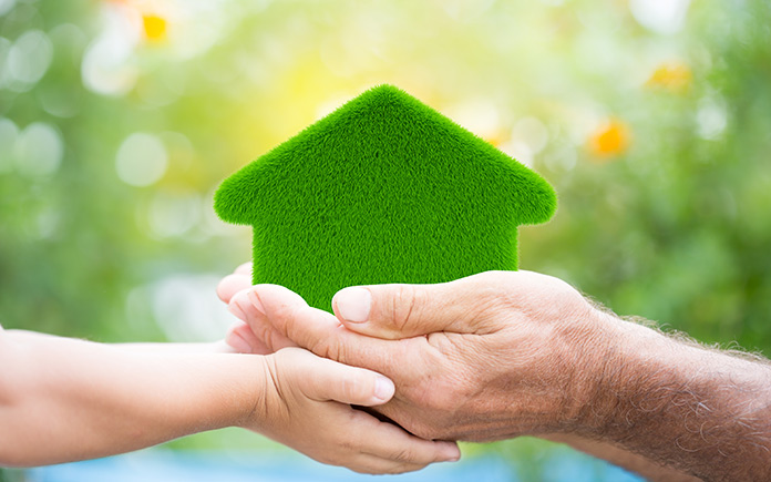 Photo illustration of a couple's hands cupping a green-colored home, symbolizing its energy efficiency