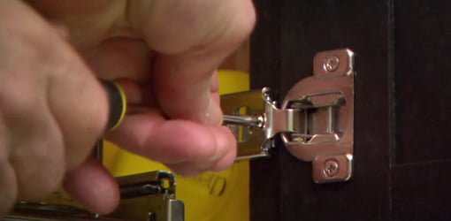 Using a screwdriver to adjust a European style cabinet hinge.