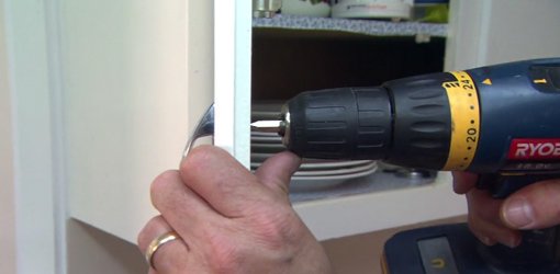 Using a cordless drill to attach cabinet handles.