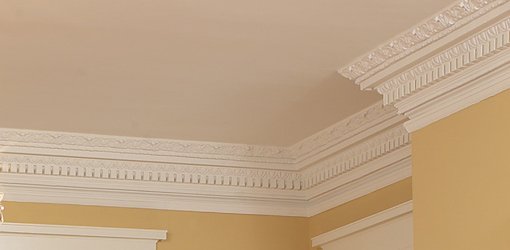 Decorative white crown molding around ceiling in room with yellow walls.
