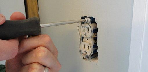 Unscrewing an electrical outlet from the box