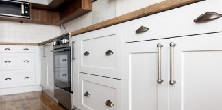 Beautiful white kitchen sink cabinet, seen from the exterior, with modern pulls and wooden floor
