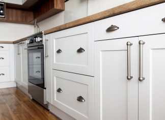 Beautiful white kitchen sink cabinet, seen from the exterior, with modern pulls and wooden floor