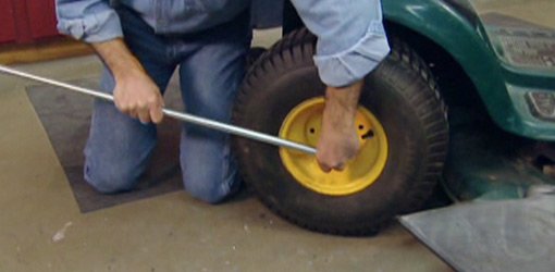 Using a pipe for a socket wrench tool handle extension to loosen a bolt on a lawn mower tractor tire.