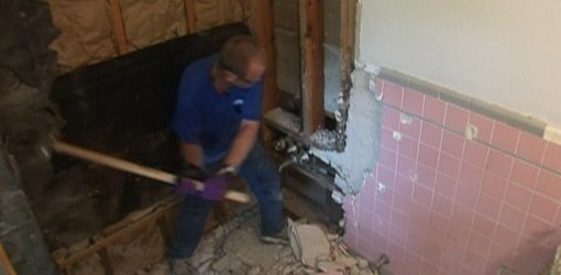Knocking tile off wall with sledgehammer.