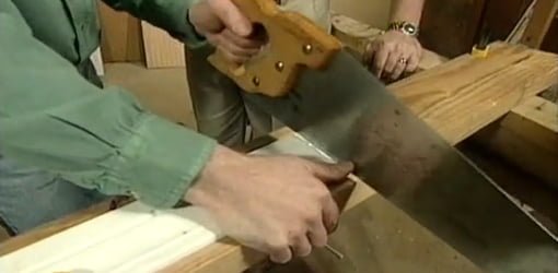 Cutting molding clamped to scrap board with handsaw.