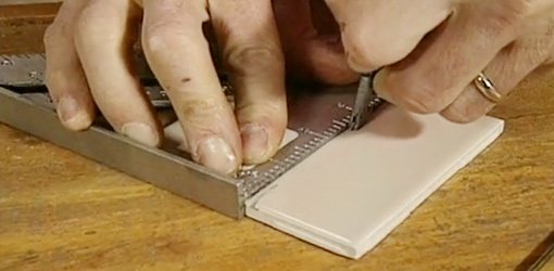 Scoring ceramic tile with a glass cutter to cut the tile to size.