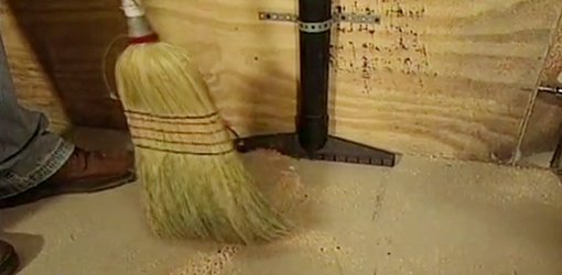Sweeping sawdust into shop vac floor nozzle mounted on wall.