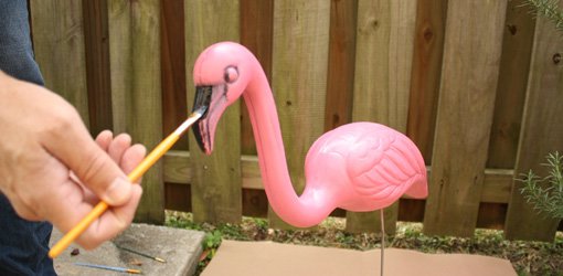 Using an artist's paintbrush to paint the accent colors on a plastic pink flamingo.