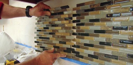 Installing a sheet of mosaic tile on a kitchen backsplash.