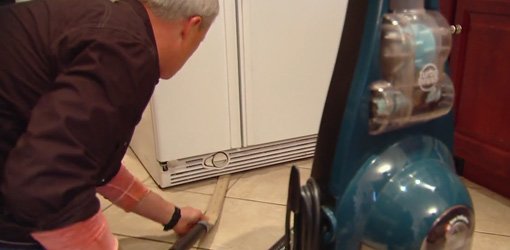 Danny Lipford using a homemade vacuum cleaner attachment to clean under the fridge.