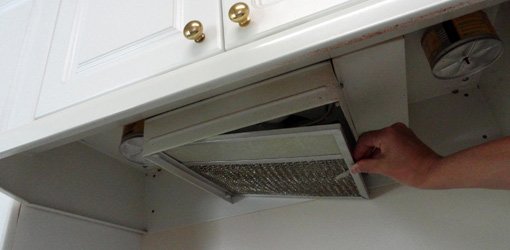 Removing the grease filter on a range hood to clean it.