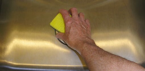 Utilizando una esponja con almohadilla abrasiva para limpiar el fregadero alrededor del agujero del colador.