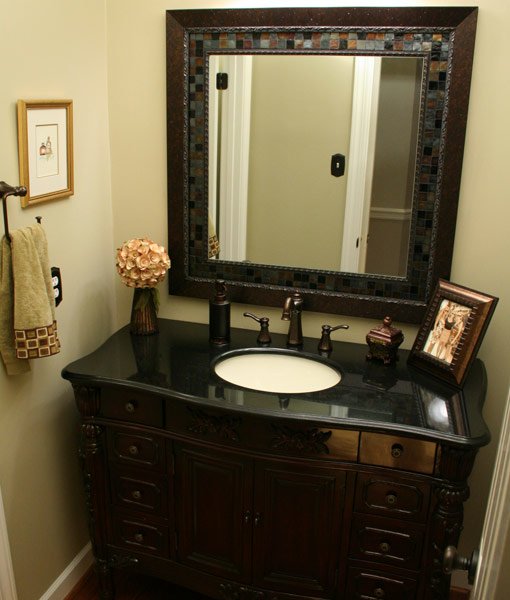 Stained wood vanity with black granite top and mosaic mirror.