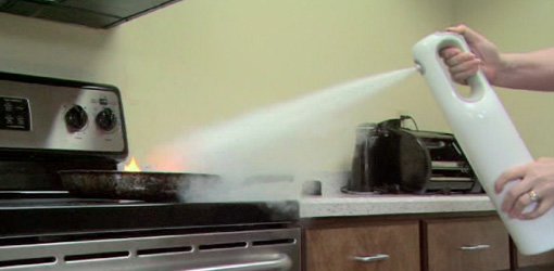 Using fire extinguisher to put out fire in frying pan on stove.