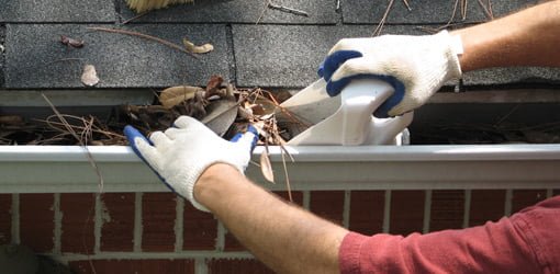 Using homemade scoop from plastic container to remove leaves from gutter.