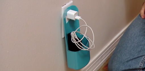 Cell phone charging station made from empty plastic bottle plugged into wall outlet.