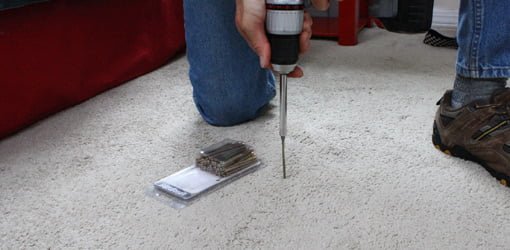 Driving a trim head screw through carpet into the subfloor to stop a squeak.