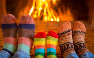Close-up of three pairs of feet, mother, father and child, with warm socks, beside a wood-burning fire