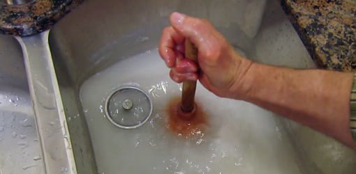 Using a plunger to unclog a kitchen sink.