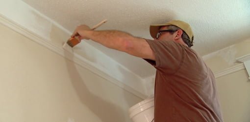 Allen Lyle using a brush to painting crown molding in a room.