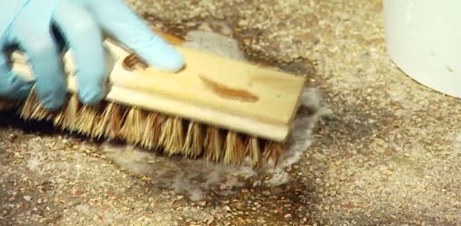 Cleaning a concrete patio with a scrub brush before staining.