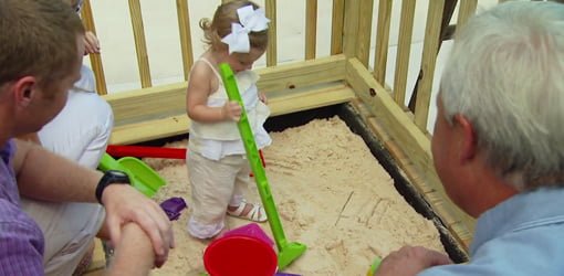 Child playing in competed wood deck sandbox.