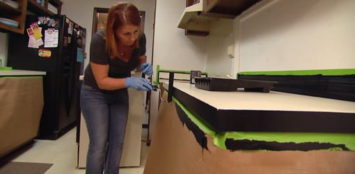Woman rolling black paint on plastic laminate kitchen countertops.