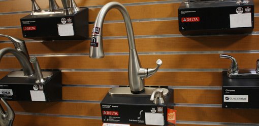 Delta Dominic kitchen faucet mounted on wall display in home center surrounded by other faucets.