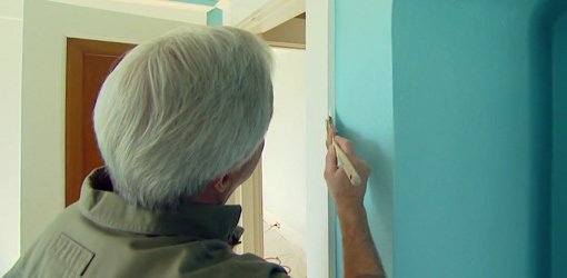 Painting white trim around a door with a paintbrush.
