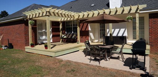 Wood deck with shade arbor pergola and concrete patio on back of brick house.