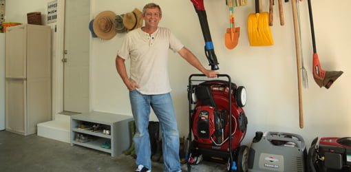 Man in garage with garden tool rack and Toro SmartStow lawn mower.