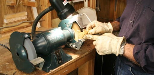 Using the wire wheel on a bench grinder to remove brass finish from hinges.