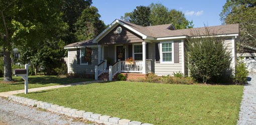 Single story ranch house with almond colored vinyl siding, brown shutters, and white trim.