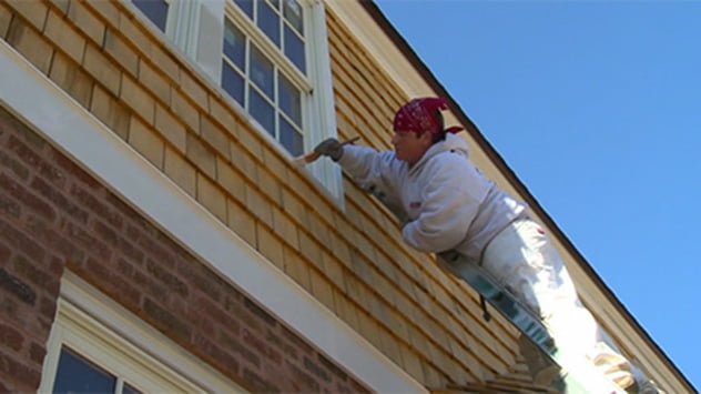 Man on ladder painting house exterior