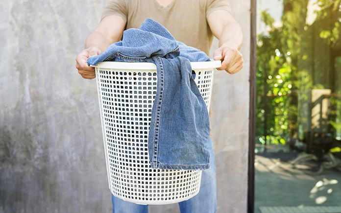 Male college student holds a laundry hamper filled with blue jeans and assorted garments