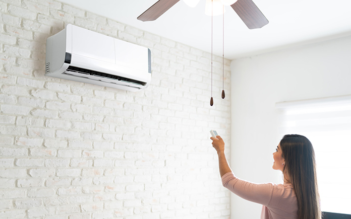 Woman controls mini split air conditioner with her remote control in a white room