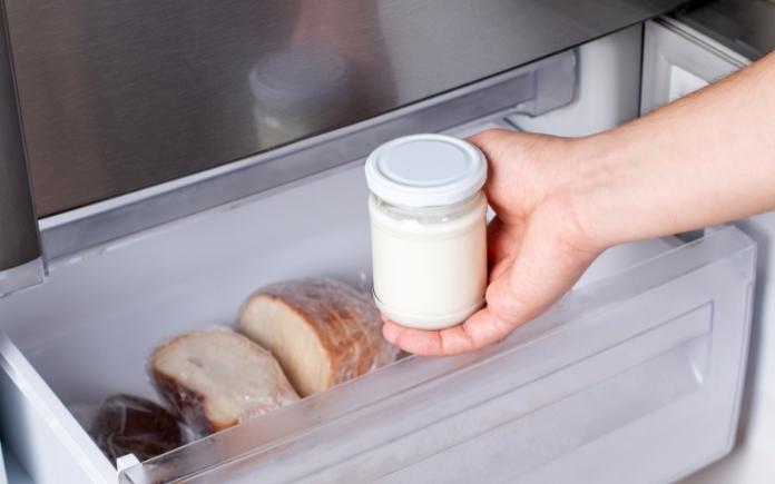 Hand placing a jar of food in freezer to preserve it
