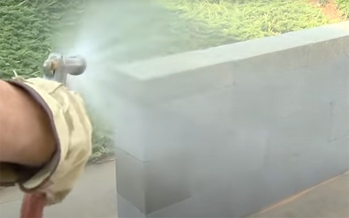 Dampening concrete blocks with a garden hose to help them cure better