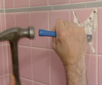 Using a hammer and cold chisel to remove a ceramic tile from a wall.