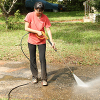 Woman using a pressure washer to clean driveway.