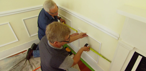 Men measuring and installing faux wainscoting on yellow wall.