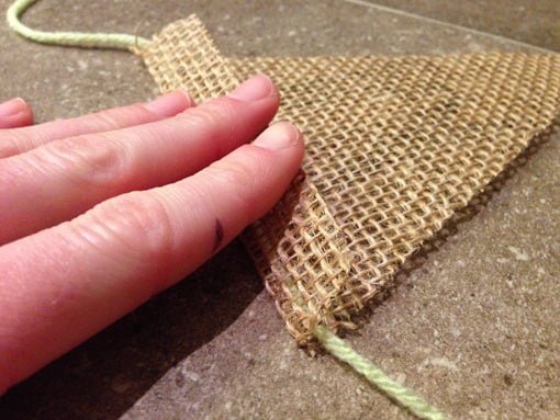 Hand holding burlap flap over yarn to be stapled