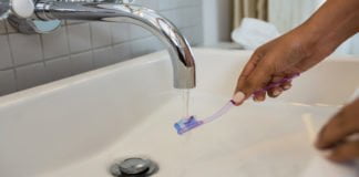 Toothbrush placed under running water in bathroom