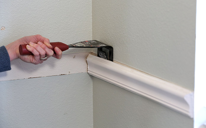 Using a trim puller to pry off wooden molding from a wall