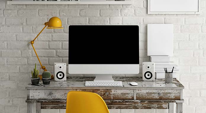 Computer with speakers on each side sitting on a desk in front of white brick walls. 